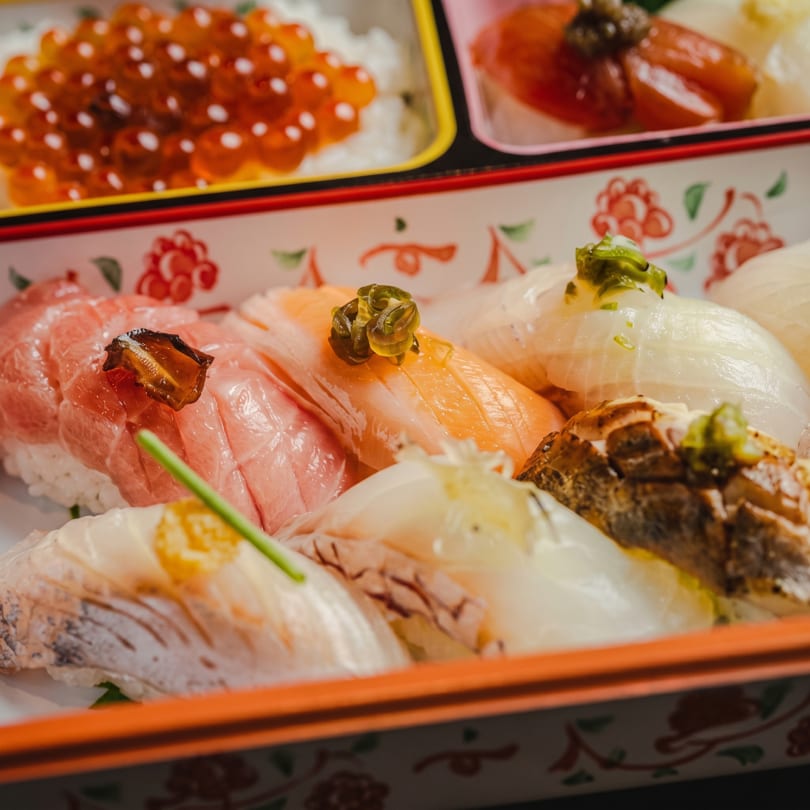 Close-up of a bento box filled with various colorful sushi pieces, including salmon and tuna.