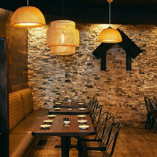 Cozy restaurant interior with bamboo pendant lights, brick wall, wooden tables, and banquette seating.