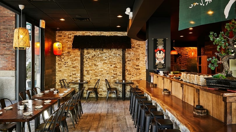 Interior of a Japanese restaurant with wooden tables, bar seating, and traditional decor.