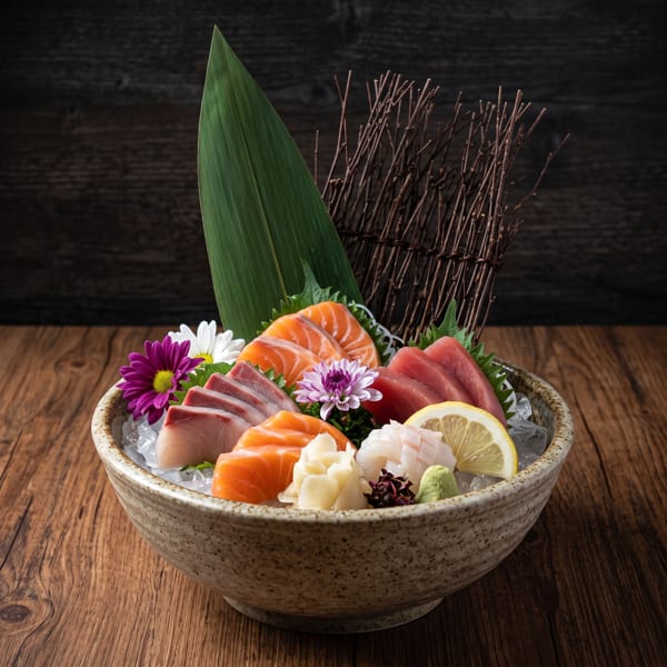 A bowl of fresh sashimi, including salmon, tuna, and white fish, garnished with flowers and lemon.