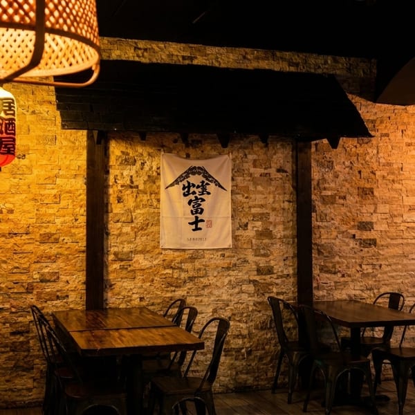 Warmly lit Japanese restaurant interior with stone walls, wooden tables, metal chairs, and hanging lanterns.