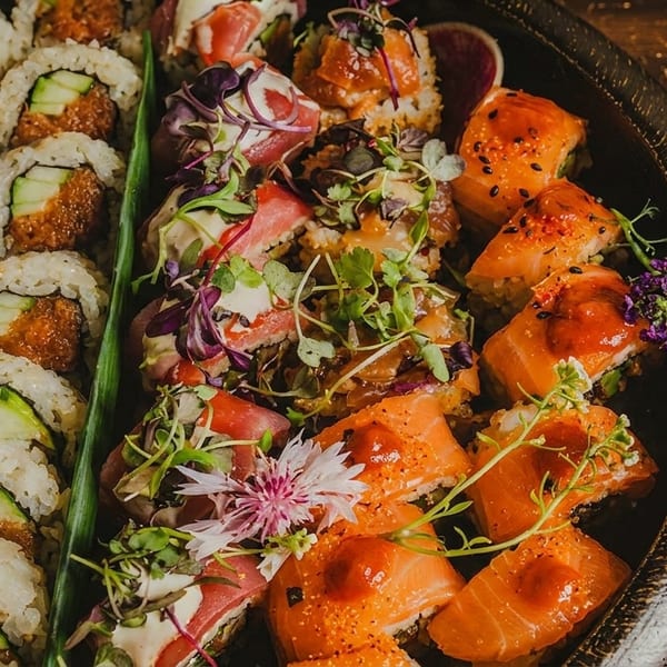 A platter of various sushi rolls, including cucumber and spicy tuna, on a dark wooden surface.