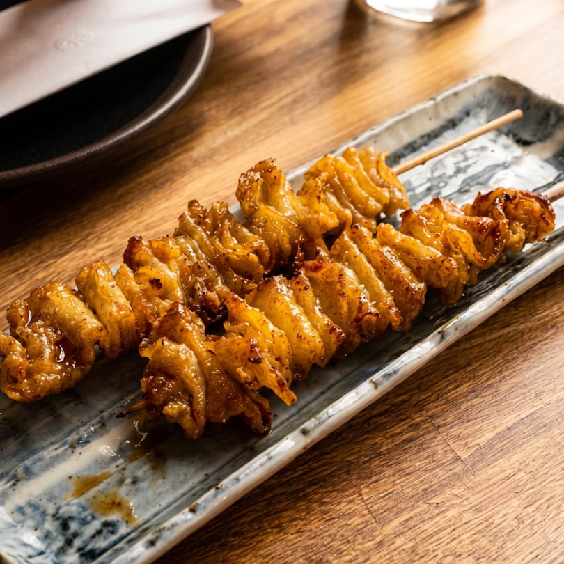 Two skewers of golden-brown grilled chicken skin yakitori on a rectangular ceramic plate.